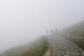 Three silhouettes of people in thick fog on rocky hiking trail in the mountains