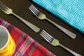 Three silver forks between blue and multicolor napkins with yellow cup on the dark reflective backdrop. Royalty Free Stock Photo