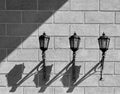 Three similar lanterns attached to the brick wall casting symmetrical shadows