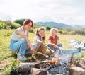 Three sisters cheerfully smiling while they roasting a marshmallows candies on the sticks over the campfire flame. Happy family or