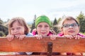 Three sisters on a mountain trip hiding behind a fence - forest and mountains in the background behind them