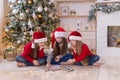 Three sisters write a letter to Santa. They are sitting near the Christmas tre