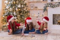 Three sisters write a letter to Santa. They are sitting near the Christmas tree