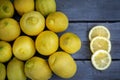 Three slices of lemon along with a group of lemons on a wood table