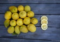 Three slices of lemon arranged with a group of lemons on a wood table