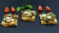Three slices of toast topped with champignon mushrooms, parsley, emmental cheese and sliced red cherry tomatoes, on slate plate