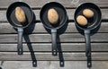 Three small aluminum pans lie side by side on a wooden slat base. In each pan there are one or two raw potatoes with their skins