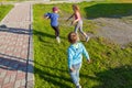 Three small children, two girls and one boy run on the green grass in the yard during the games, chasing each other to take away Royalty Free Stock Photo