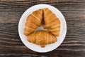 Three small croissants in white plate on dark wooden table Royalty Free Stock Photo