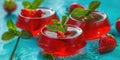 Three small red jello cups with green mint leaves and strawberries on top Royalty Free Stock Photo