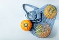 Three small ripe beautiful pumpkins lie in a blue eco-friendly string bag on a gray background