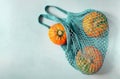 Three small ripe beautiful pumpkins lie in a turquoise eco-friendly string bag on a gray background