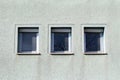 Three small windows in a row with tree branches in reflection and white plastic frame covered with dust and cobwebs