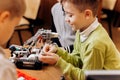 Three smart boys are making robots from the robotic constructor at the desk with computer in the School of Robotics
