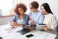 Three smart students are sitting together and studying. Guy wears glasses and looking to the girl`s phone while the