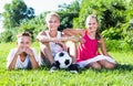 Three smiling kids with ball resting on grass on summer day Royalty Free Stock Photo