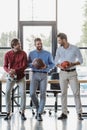 three smiling young businessmen holding basketball soccer and rugby balls