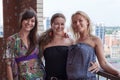 Three smiling women a friends standing and embracing together on building balcony