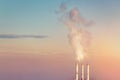 Three smoking stack pipes making clouds of white smoke with dramatic sunset sky background. Industrial minimalistic landscape.