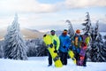 Three snowboarders posing at ski resort. Friends climbing to mountain top carrying their snowboards through forest for