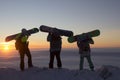 Three snowboarders standing on top of a mountain at dawn