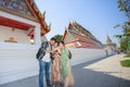 Three South Asian tourists happily stand by looking at a photo from a mobile phone behind Wat Pho during a long weekend. in