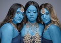 Three South Asian women painted blue and wearing gold jewellery