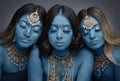 Three South Asian women painted blue and wearing gold jewellery