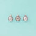 Three sparkly silver Christmas baubles on a blue green background, with copy space