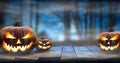 Three spooky halloween pumpkins, Jack O Lantern, with evil face and eyes on a wooden bench