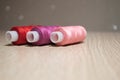 Three spools of thread, red, pink and crimson, on table