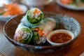 Three spring rolls filled with rice noodles, carrots, and greens, rest on a brown bowl with a dipping sauce dish, Spring rolls