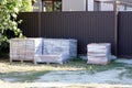 Three square boxes in plastic packaging with paving bricks stand on gray ground near the brown metal fence Royalty Free Stock Photo