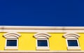 Three square windows on a yellow building with bright blue sky i Royalty Free Stock Photo