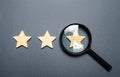 Three stars and a magnifying glass on a gray background. Authentication of the third star, rating fraud. Rating and status of the