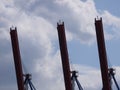 Three steel, rust-painted, outriggers of harbor cranes.