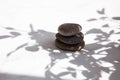 Three stones are stacked one on top of the other in the shadows of leaves and sunlight on a white marble background Royalty Free Stock Photo