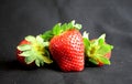 Three strawberries lying/standing on black fabric