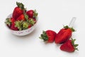 Three strawberries, one of them on a spoon and next to it a bowl with more strawberries