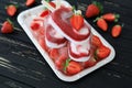 Three strawberry vanilla ice cream popsicles on ice cubes and strawberry slices on the black wooden background. Royalty Free Stock Photo