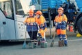 Three street female cleaners in municipal uniform and orange helmets with brooms stand with different emotions for short break