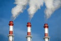 Three striped industrial pipes with smoke over cloudless blue sky Royalty Free Stock Photo