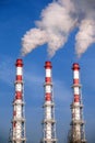 Three striped industrial pipes with smoke over cloudless blue sky Royalty Free Stock Photo