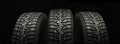 Three studded winter tires wheels in a row on a black background, panoramic shot