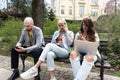 Three students on a bench in the park study talking typing on laptop notebook and writing. Education concept. Young colleagues Royalty Free Stock Photo