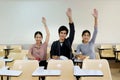 Three students raised their hands together in the classroom.