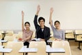 Three students raised their hands together in the classroom.
