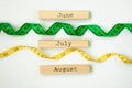 Three summer month - June, July and August - on wooden blocks with centimeter tape isolated on white