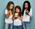 Three surprised socked kids girls friends in white t-shirts stand looking at glasses of water, milk and fresh juice