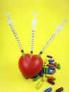 Three syringes pined to a red spongy heart with pills